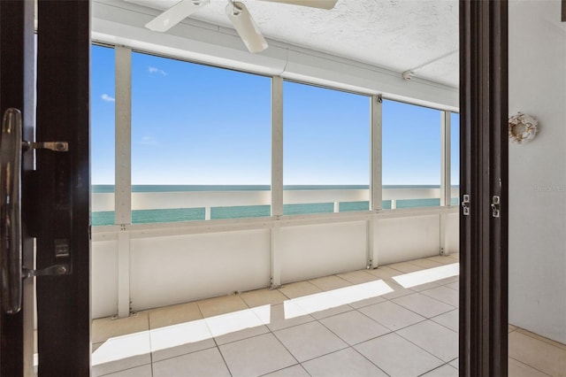 unfurnished sunroom featuring a view of the beach, ceiling fan, and a water view