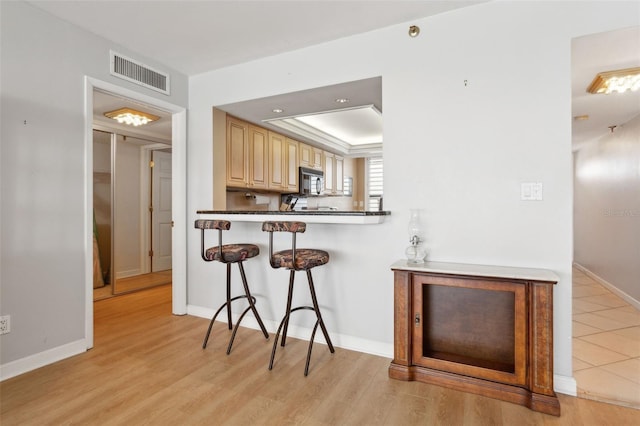 kitchen featuring a kitchen bar, light brown cabinets, kitchen peninsula, and light wood-type flooring