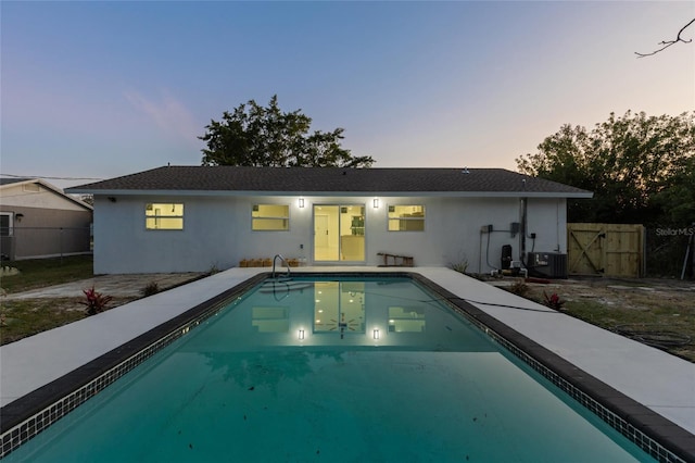 back house at dusk featuring a fenced in pool and central AC