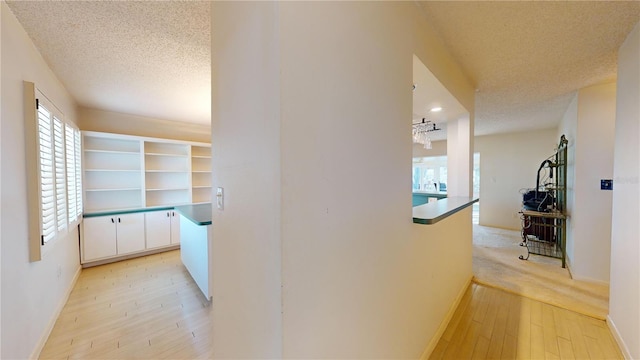 hall with light wood-type flooring and a textured ceiling