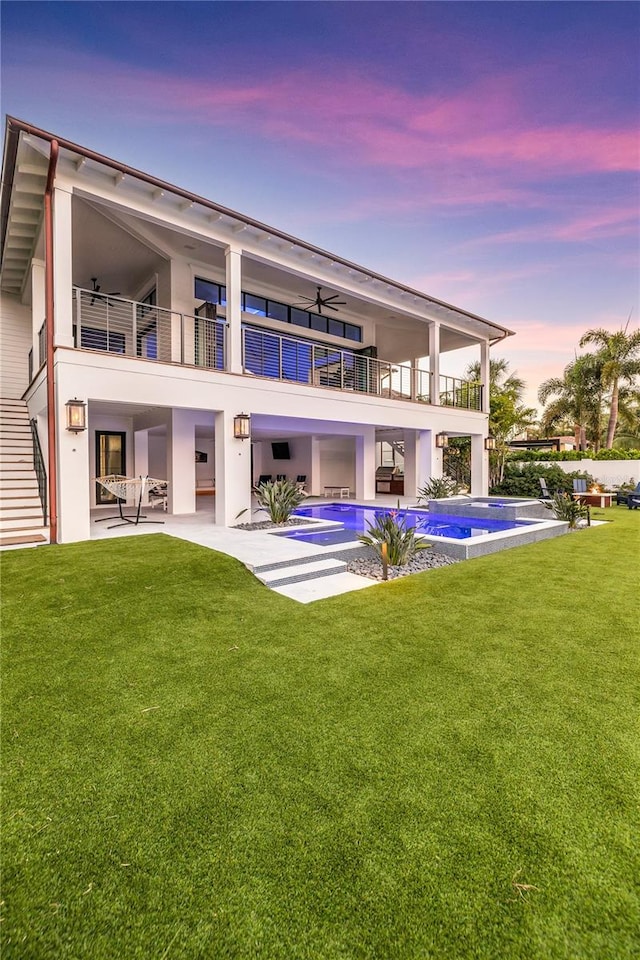 rear view of property featuring a swimming pool with hot tub, a yard, a patio, and a balcony