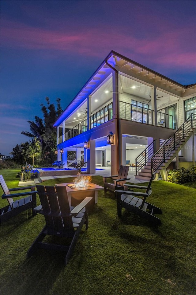 back house at dusk featuring an outdoor fire pit and a lawn