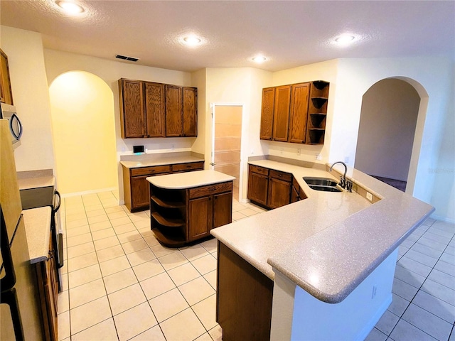 kitchen featuring a kitchen island, sink, light tile patterned floors, kitchen peninsula, and a textured ceiling