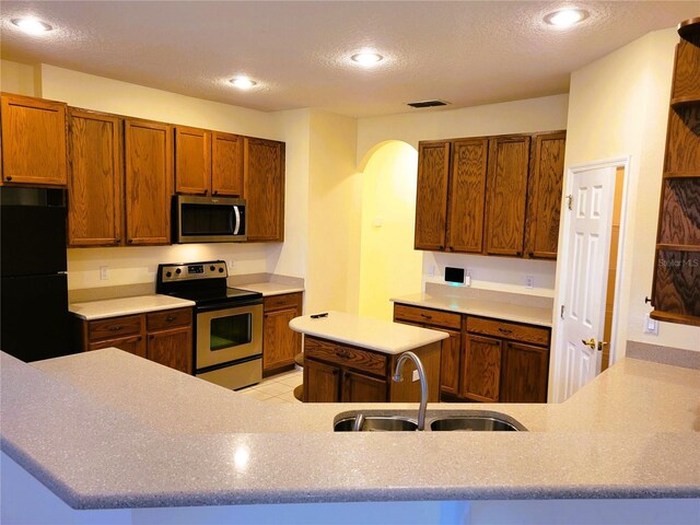 kitchen featuring appliances with stainless steel finishes, sink, light tile patterned floors, kitchen peninsula, and a textured ceiling