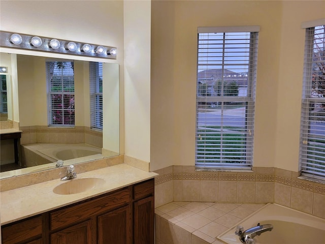 bathroom featuring vanity, a healthy amount of sunlight, and a relaxing tiled tub