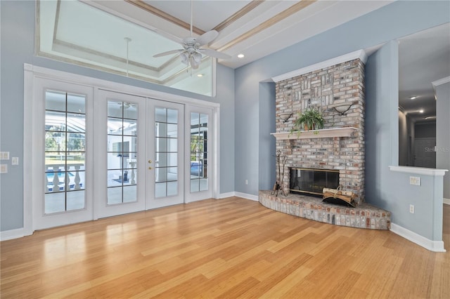 unfurnished living room featuring a brick fireplace, a tray ceiling, ornamental molding, and light hardwood / wood-style floors