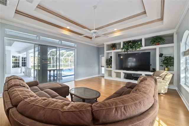 living room with a raised ceiling, crown molding, and light hardwood / wood-style flooring