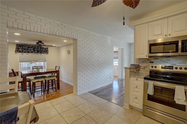 kitchen with backsplash, light tile patterned floors, light stone counters, ceiling fan, and stainless steel appliances