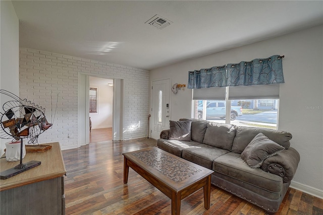 living room featuring dark wood-type flooring and brick wall