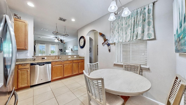 kitchen with light tile patterned flooring, sink, light stone counters, hanging light fixtures, and appliances with stainless steel finishes