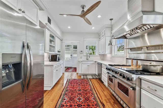 kitchen with white cabinetry, stainless steel appliances, hanging light fixtures, and island range hood