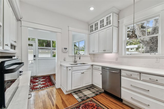 kitchen featuring pendant lighting, sink, light hardwood / wood-style flooring, white cabinets, and stainless steel dishwasher