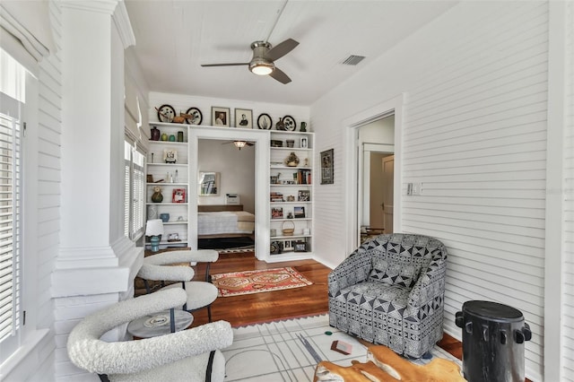 living area with decorative columns, plenty of natural light, hardwood / wood-style floors, and ceiling fan