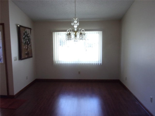 spare room with dark hardwood / wood-style floors, a chandelier, and a textured ceiling