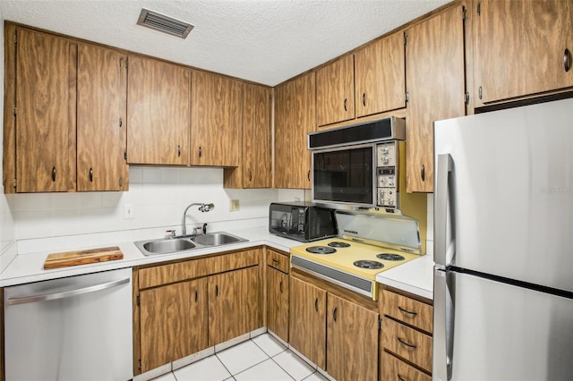 kitchen featuring appliances with stainless steel finishes, tasteful backsplash, sink, light tile patterned floors, and a textured ceiling