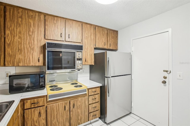 kitchen featuring sink, stainless steel refrigerator, a textured ceiling, light tile patterned flooring, and cooktop