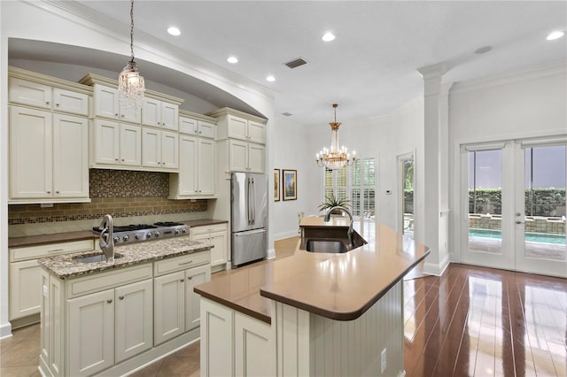 kitchen featuring sink, appliances with stainless steel finishes, decorative backsplash, a center island with sink, and decorative light fixtures