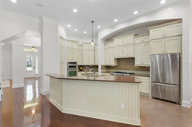 kitchen featuring decorative backsplash, stainless steel appliances, an island with sink, and hanging light fixtures