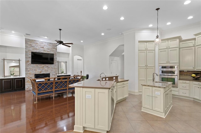 kitchen with cream cabinets, decorative light fixtures, stainless steel double oven, and a center island with sink