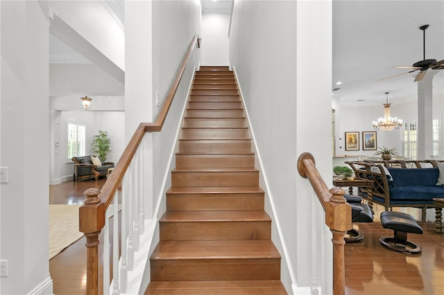 stairs with hardwood / wood-style flooring, crown molding, and ceiling fan with notable chandelier