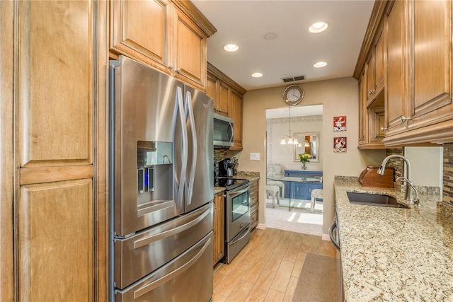 kitchen featuring sink, light stone counters, decorative light fixtures, light hardwood / wood-style flooring, and appliances with stainless steel finishes