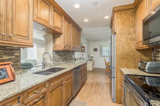 kitchen featuring sink, tasteful backsplash, light wood-type flooring, stainless steel appliances, and light stone countertops