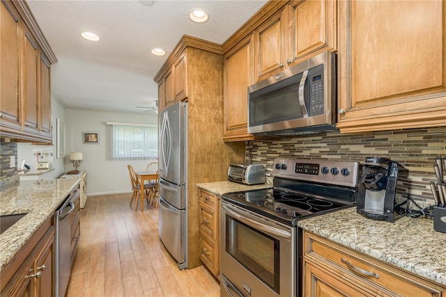 kitchen with light stone counters, backsplash, light wood-type flooring, and appliances with stainless steel finishes