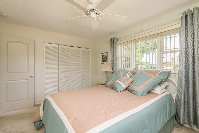 bedroom featuring ceiling fan, light colored carpet, a closet, and a textured ceiling