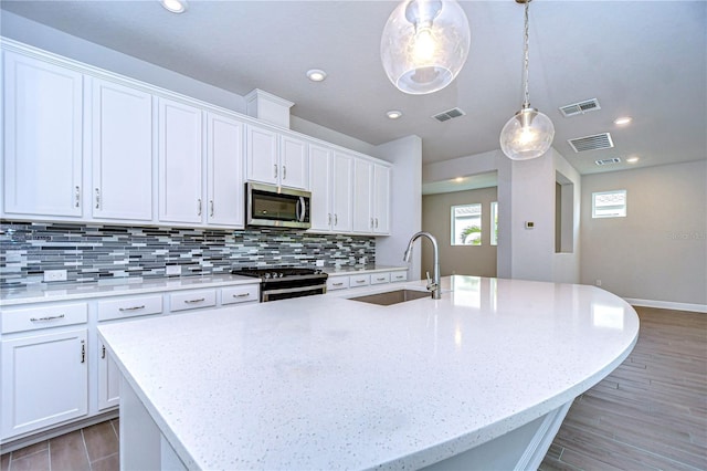 kitchen featuring stove, sink, a kitchen island with sink, and white cabinets