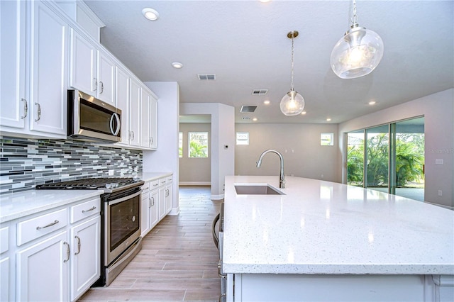 kitchen with white cabinetry, appliances with stainless steel finishes, a kitchen island with sink, and sink