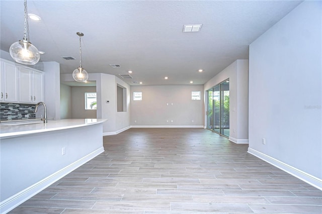 kitchen featuring decorative backsplash, white cabinets, light wood-type flooring, and decorative light fixtures