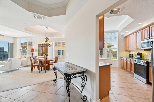 kitchen featuring light tile patterned flooring, appliances with stainless steel finishes, decorative light fixtures, a raised ceiling, and crown molding