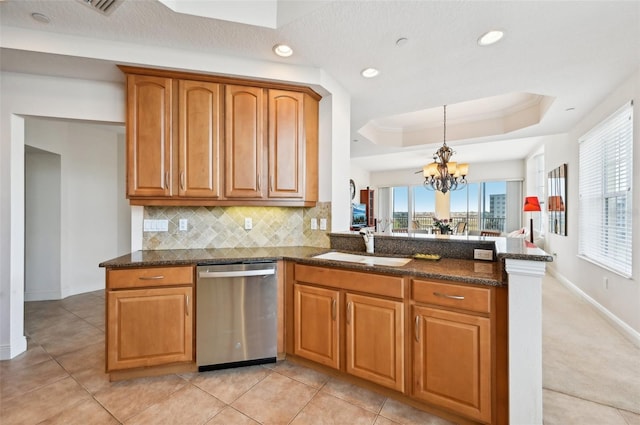 kitchen featuring sink, dark stone countertops, a tray ceiling, dishwasher, and decorative backsplash