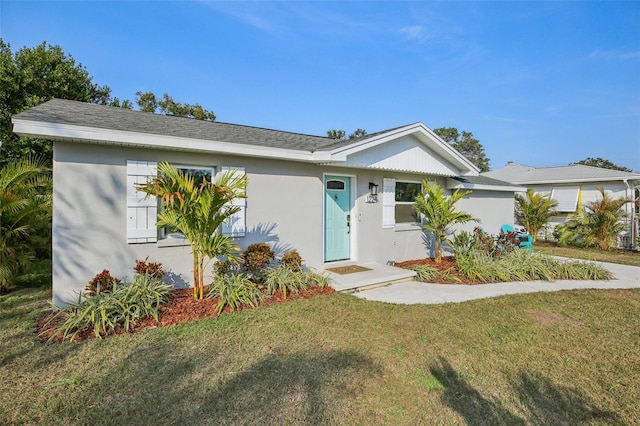 view of front of house with roof with shingles, a front yard, and stucco siding