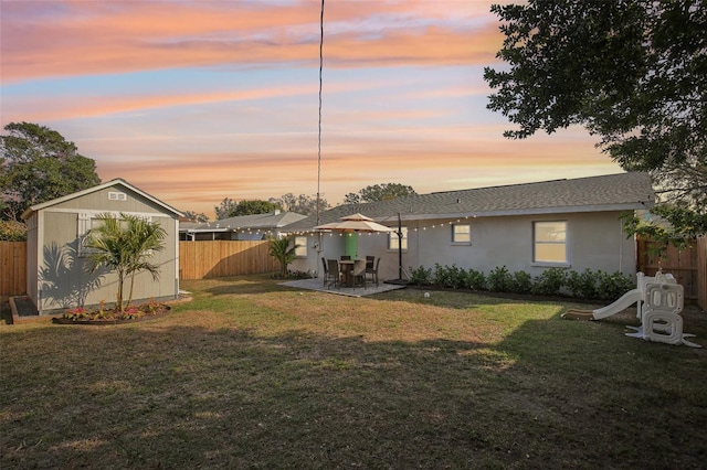 back of house at dusk featuring a patio, an outdoor structure, fence, a yard, and a storage unit