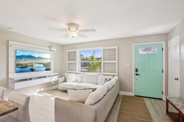 living room featuring a textured ceiling, baseboards, a ceiling fan, and light wood-style floors