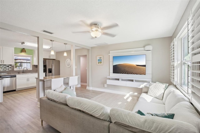 living room with visible vents, a ceiling fan, a textured ceiling, light wood-type flooring, and baseboards