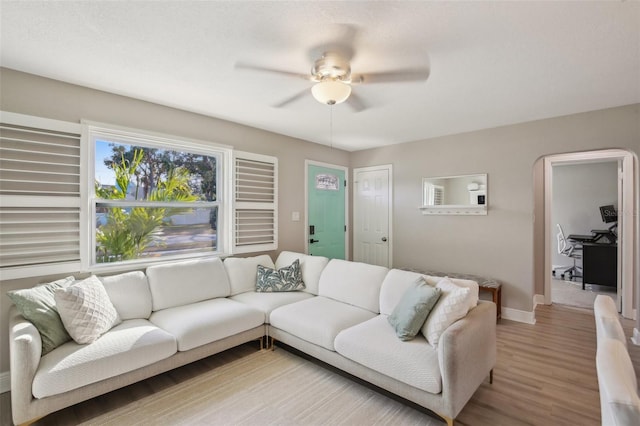 living room with light wood finished floors, baseboards, arched walkways, and a ceiling fan