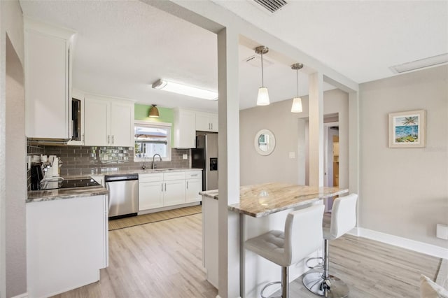 kitchen with tasteful backsplash, white cabinets, hanging light fixtures, stainless steel appliances, and a sink