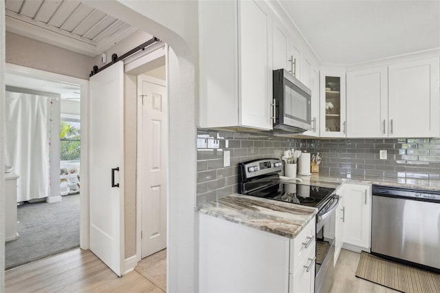 kitchen with stainless steel appliances, a barn door, glass insert cabinets, white cabinetry, and light stone countertops