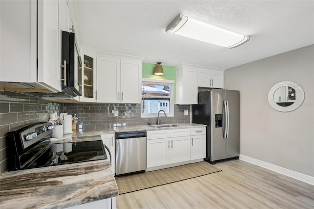 kitchen featuring appliances with stainless steel finishes, glass insert cabinets, white cabinetry, a sink, and light stone countertops