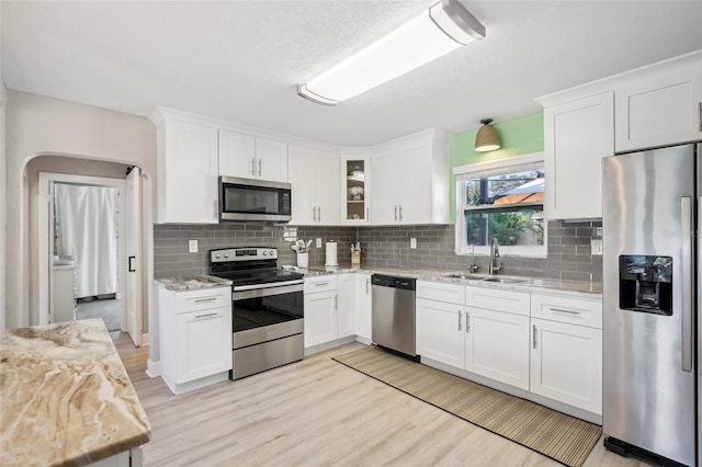 kitchen featuring light stone counters, appliances with stainless steel finishes, glass insert cabinets, white cabinets, and a sink