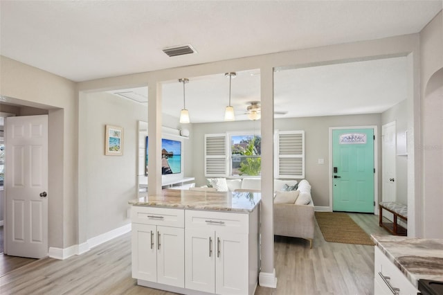 kitchen featuring light stone counters, visible vents, white cabinetry, light wood-type flooring, and decorative light fixtures