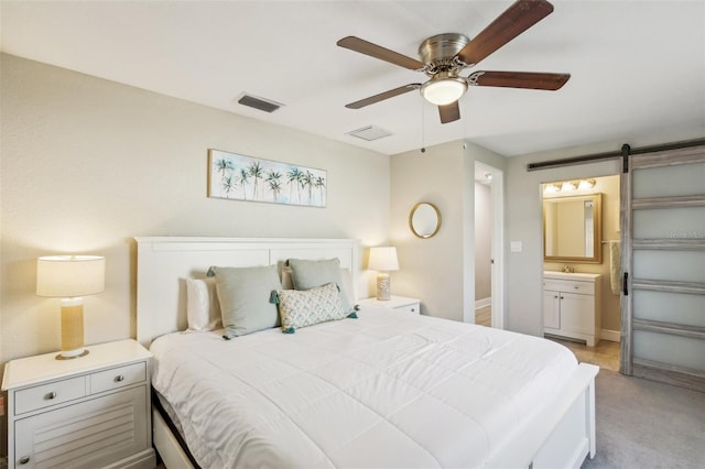 bedroom with ceiling fan, a barn door, connected bathroom, light carpet, and visible vents