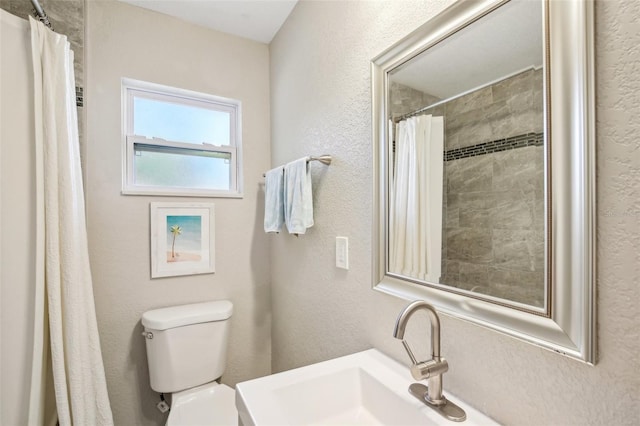 full bathroom featuring a textured wall, tiled shower, a sink, and toilet