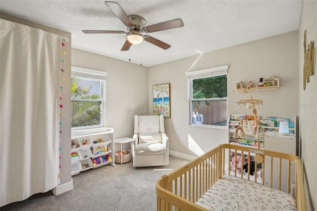 bedroom with baseboards, a ceiling fan, carpet, a textured ceiling, and a nursery area