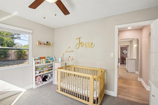 bedroom featuring a crib, baseboards, arched walkways, and carpet flooring