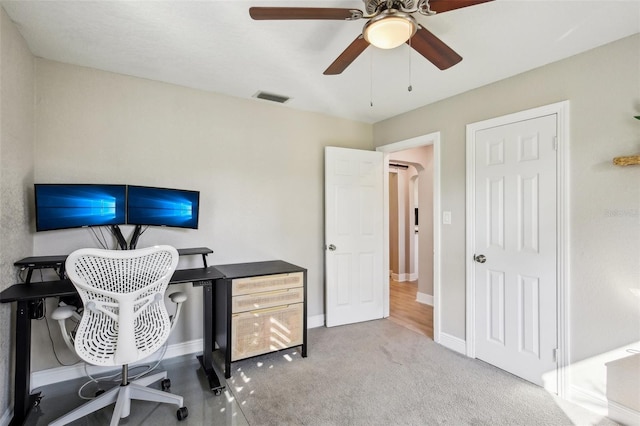 carpeted office space with ceiling fan, arched walkways, visible vents, and baseboards