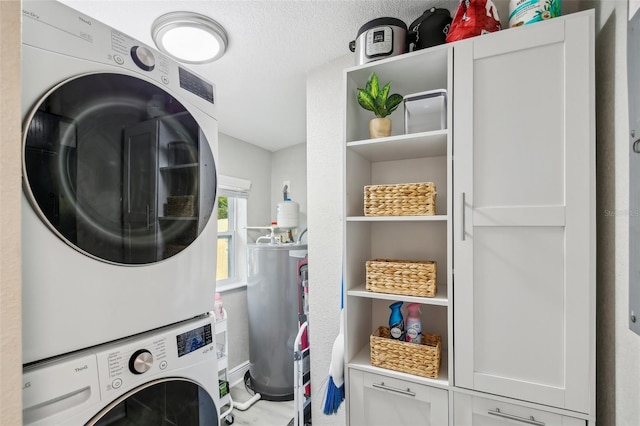 laundry area featuring cabinet space, a textured ceiling, stacked washing maching and dryer, and water heater