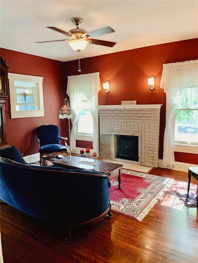 living room with a brick fireplace, wood-type flooring, and ceiling fan